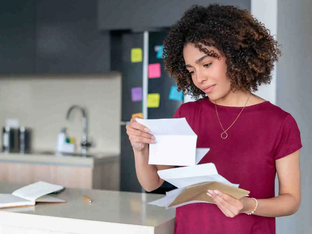 Woman reading mail in the kitchen with a confused expression