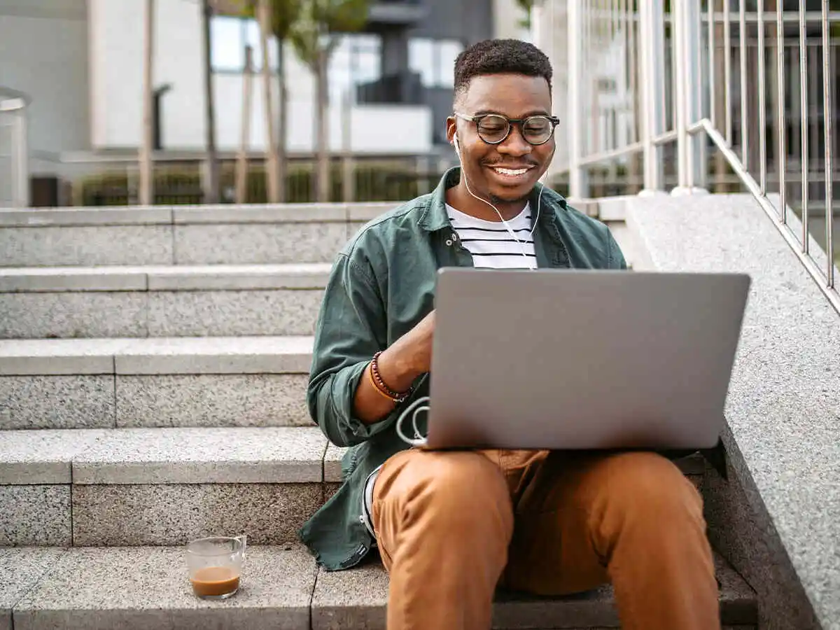 Man sitting on step listening to music and smiling at laptop