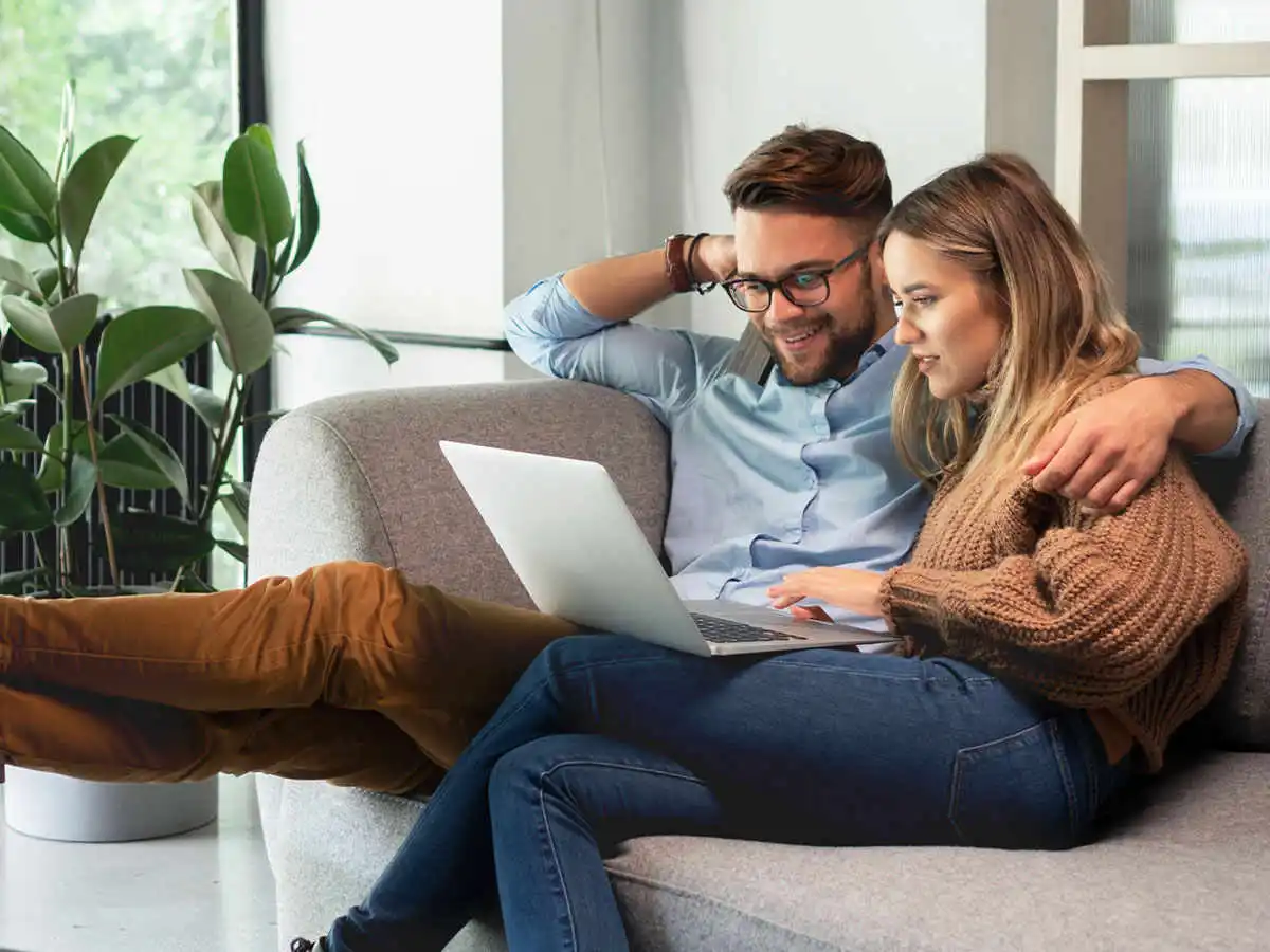 Man with arm around woman on couch looking at a laptop