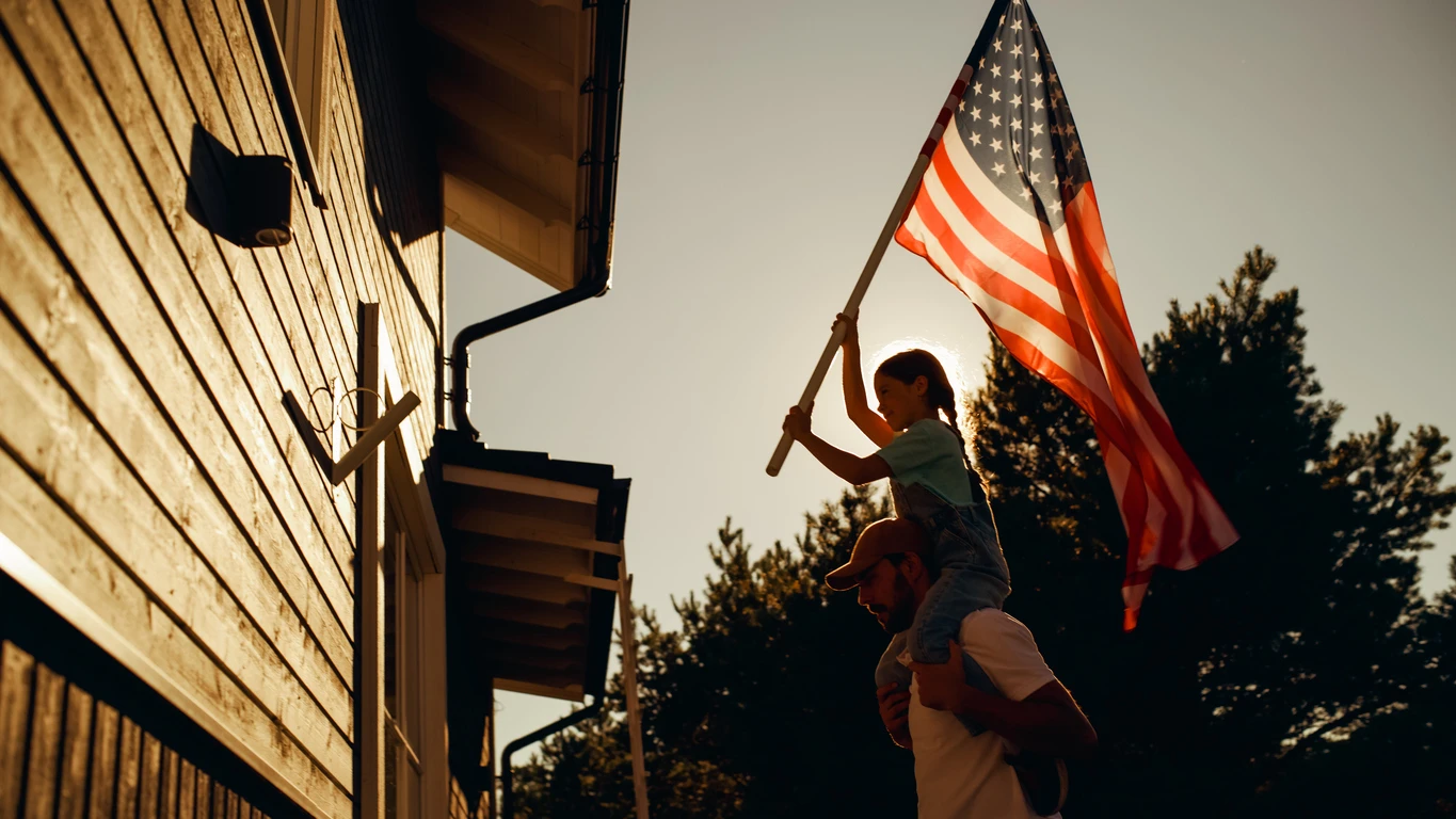 Father holding his daughter on his shoulders while she places an american flag