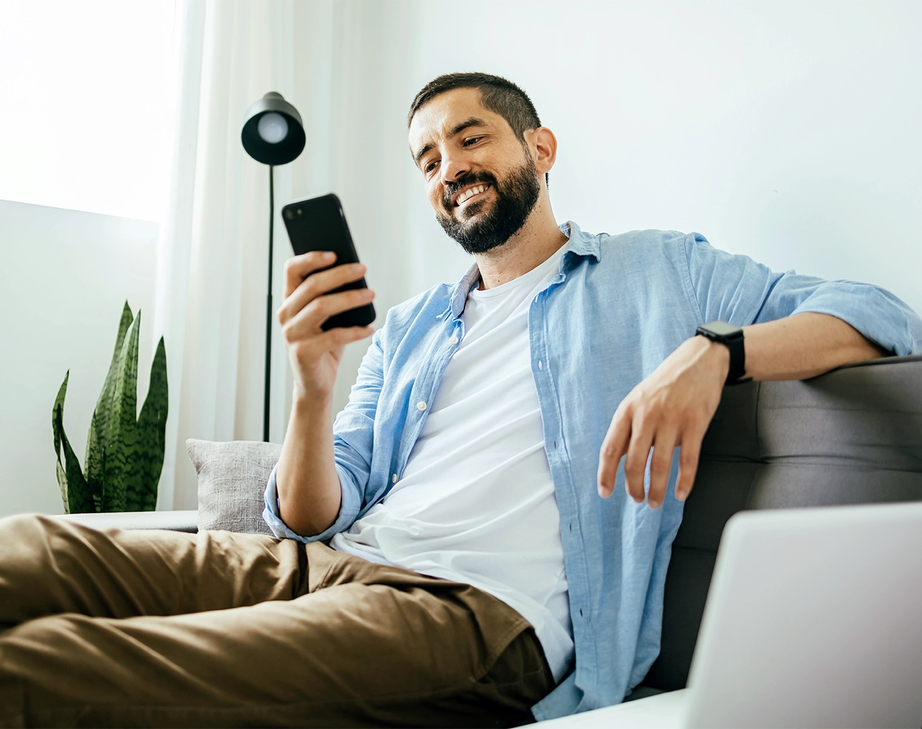 happy man using phone at home sitting on sofa