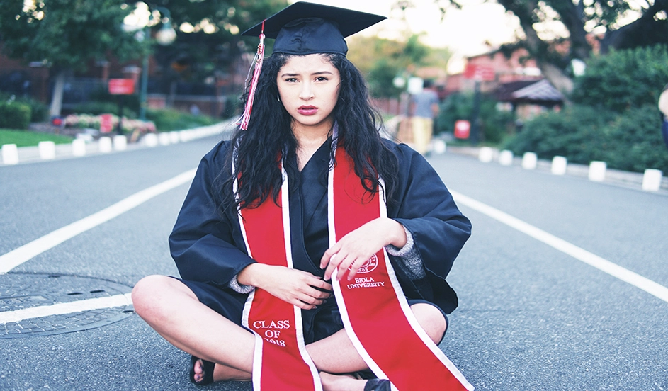 Woman sitting in road wearing graduation cap and gown