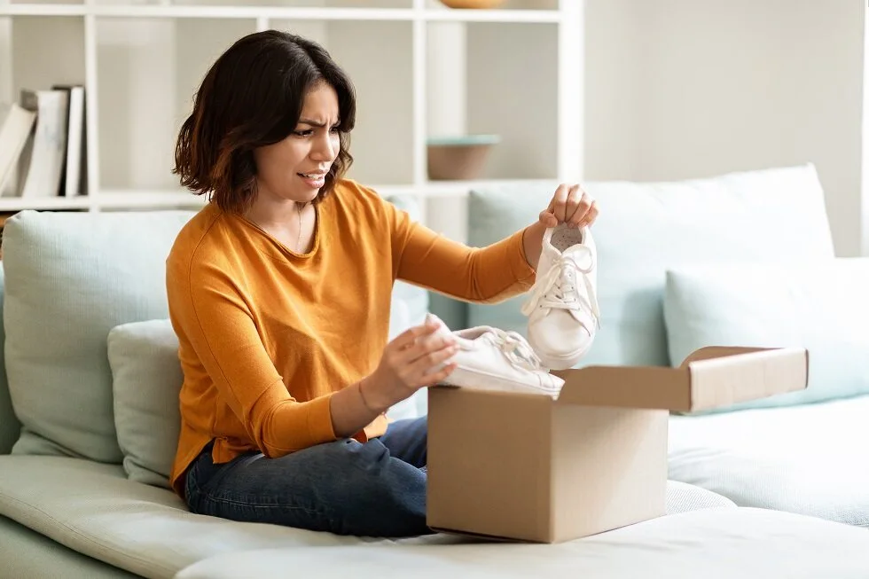 Woman sitting on couch opening package and confused with contents