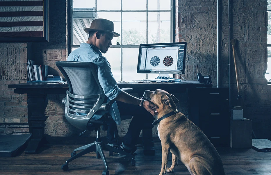 Man sitting at desk looking at computer and petting dog