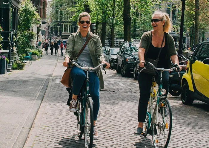 Two people riding bikes down the sidewalk in the Netherlands