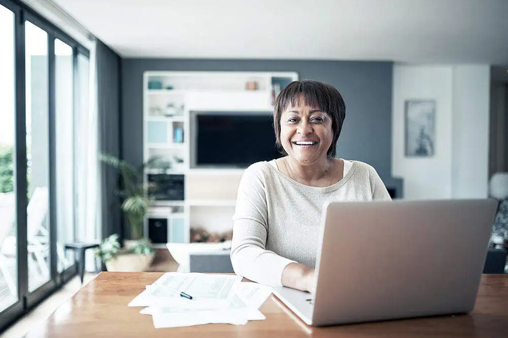 Woman smiling working on her laptop with papers on her desk