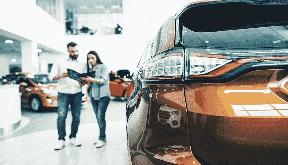 Man and woman looking over a car catalogue with the back of a car in the foreground
