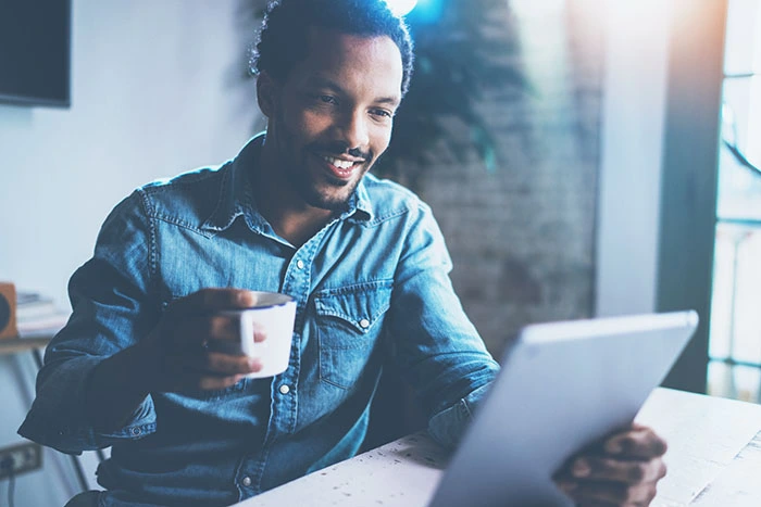 Man smiling at a tablet while drinking coffee