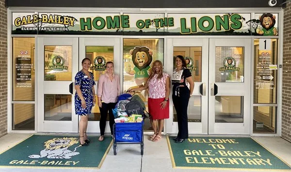 AFCU members standing in front of a school with donation bin