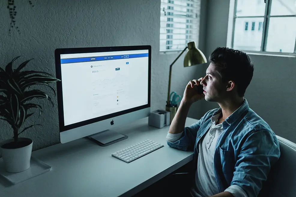 Man on the phone looking at his desktop computer screen