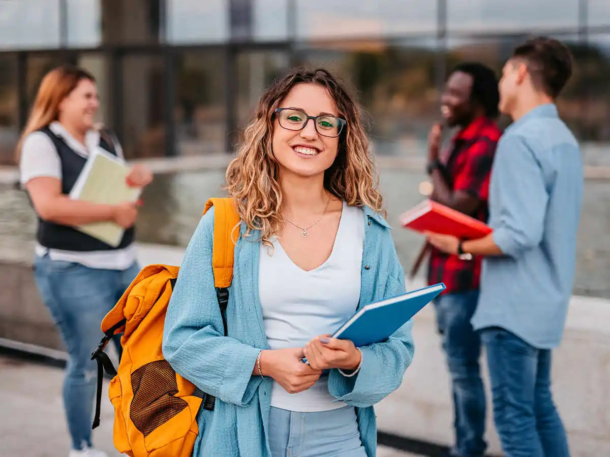 Woman with backpack and book smiling with peers in the background