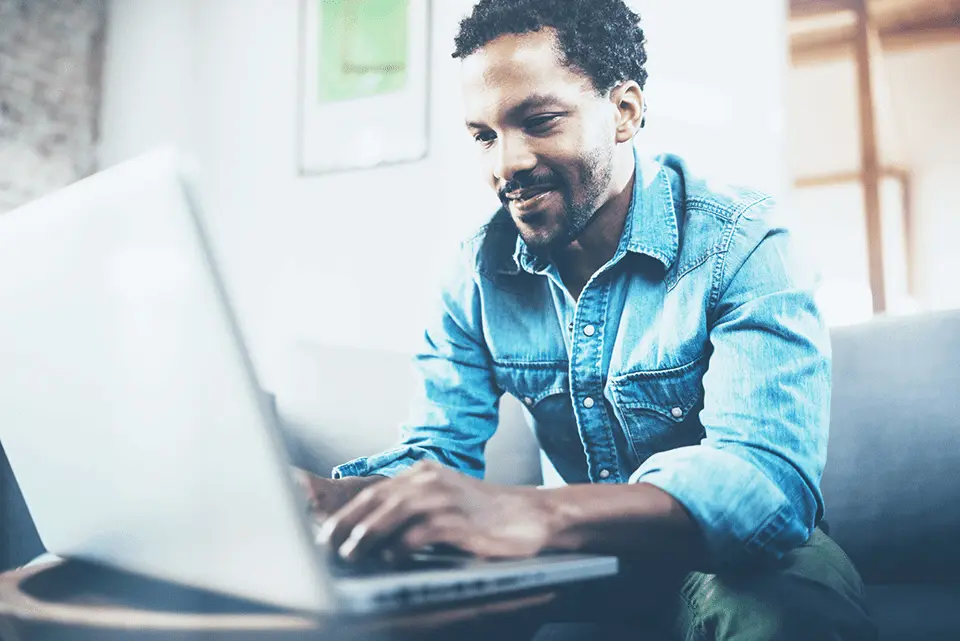 Man on a couch smiling down at a laptop